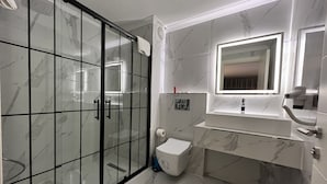 Un baño moderno con cabina de ducha de vidrio, suelo de baldosas de mármol, un lavabo blanco con un espejo encima y un inodoro.