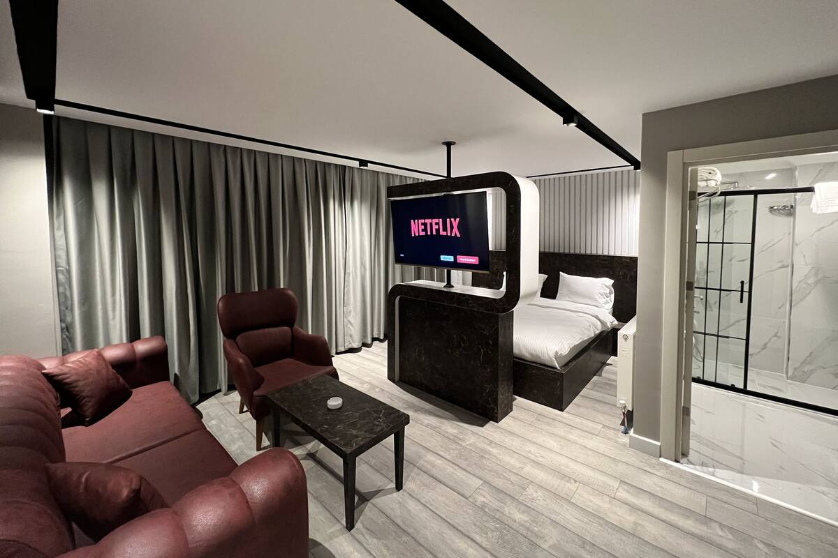 A modern hotel room with a large bed, a seating area with a table, a TV displaying 'NETFLIX', and a shower area.