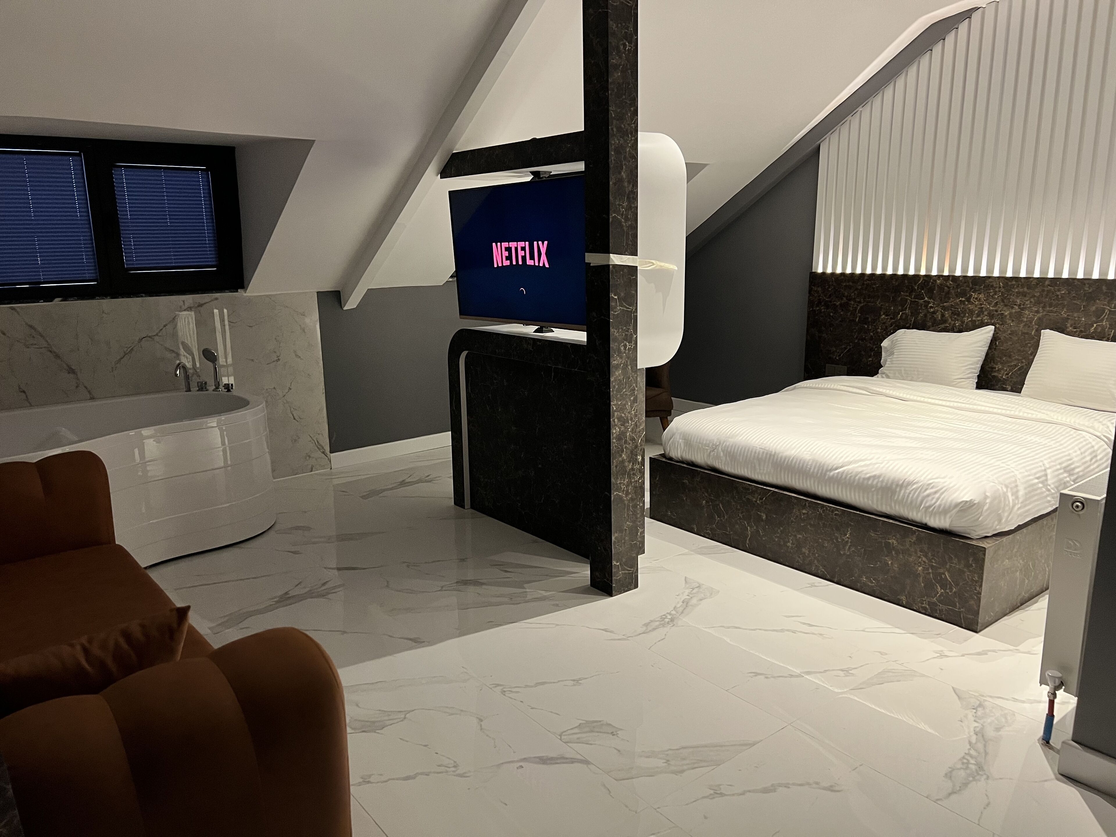 Une chambre moderne avec un grand lit, un téléviseur affichant le logo « NETFLIX », une baignoire et un sol en marbre.