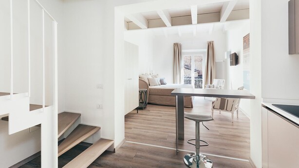 Un interior moderno con una escalera, una zona de comedor y un espacio de estar con sofá y cortinas.
