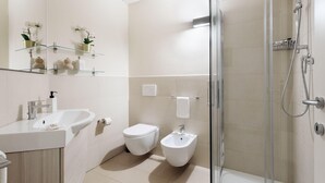 Un baño moderno con cabina de ducha de vidrio, lavamanos blanco, inodoro y bidé.