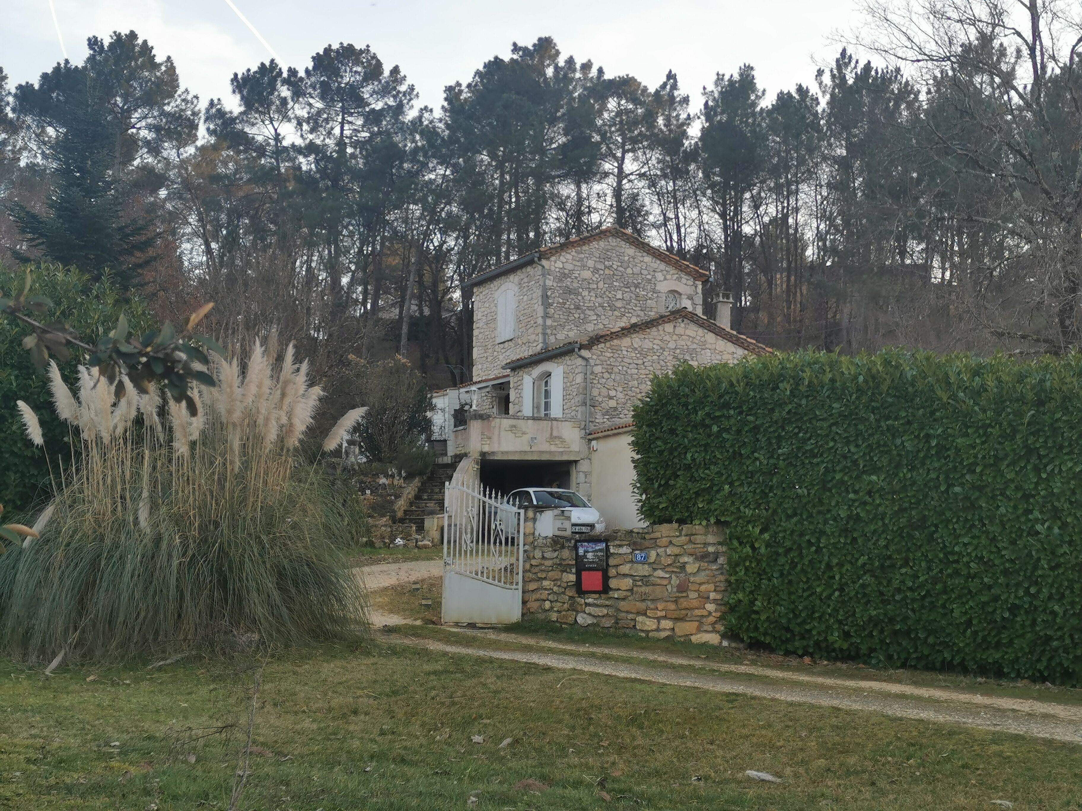 A stone building with a white gate, surrounded by greenery and trees.