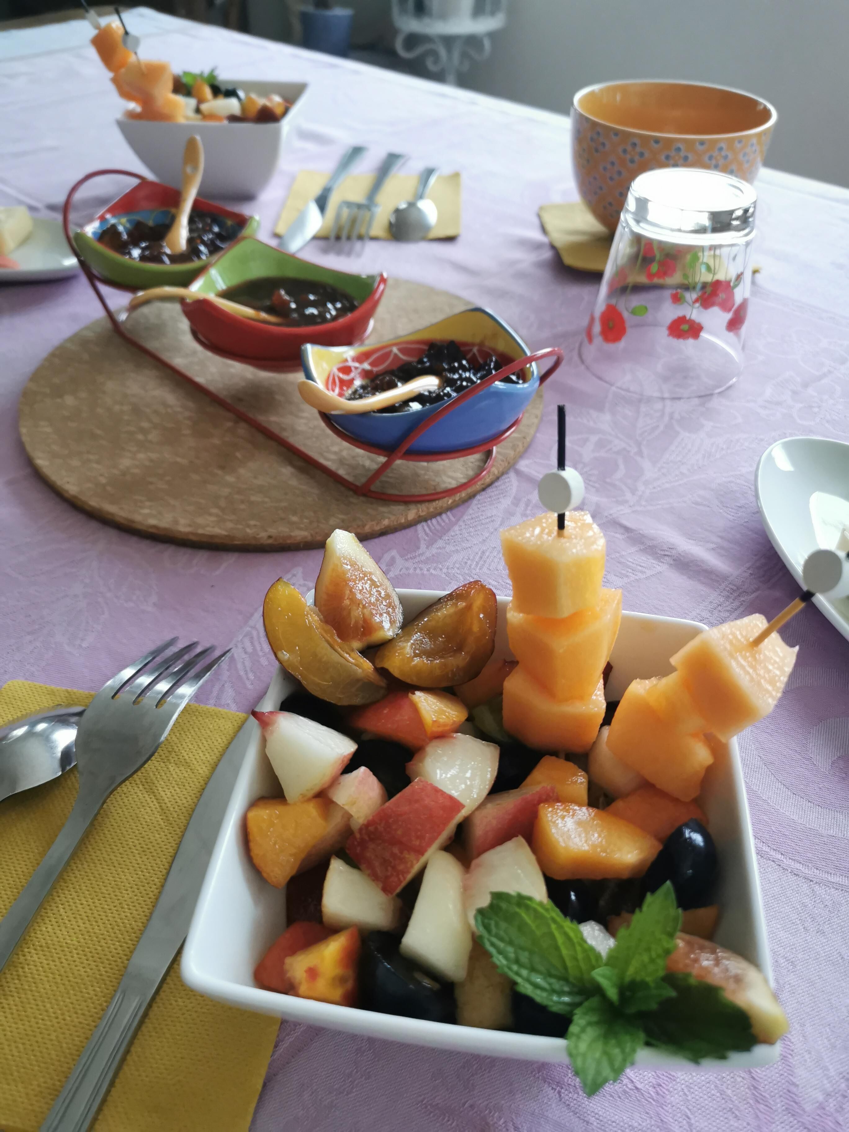 Una mesa con frutas variadas y un tazón pequeño que parece ensalada de frutas.