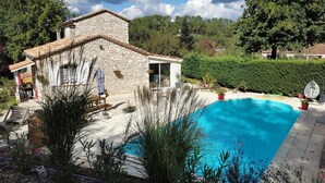 Una casa de piedra con piscina, rodeada de vegetación y árboles.