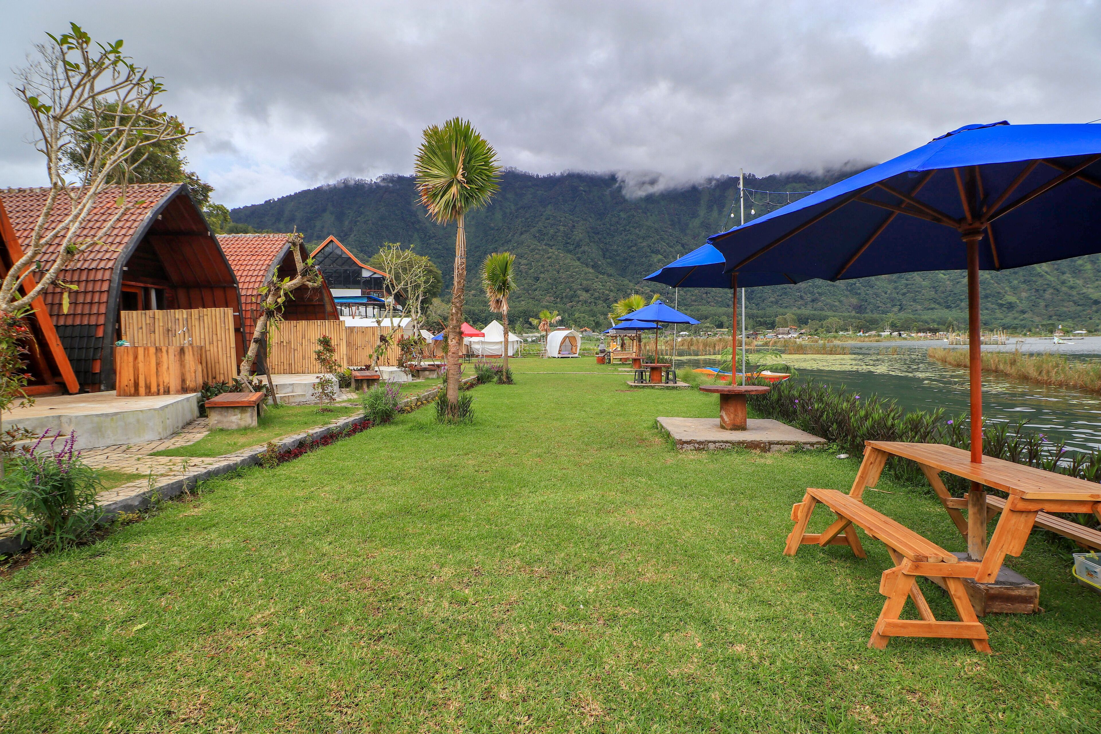 Un camping con cabañas de madera, mesas de picnic y sombrillas.