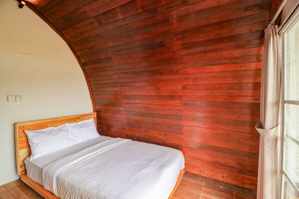 Una habitación con techo inclinado de madera, una cama con ropa blanca y un ventanal con cortinas.