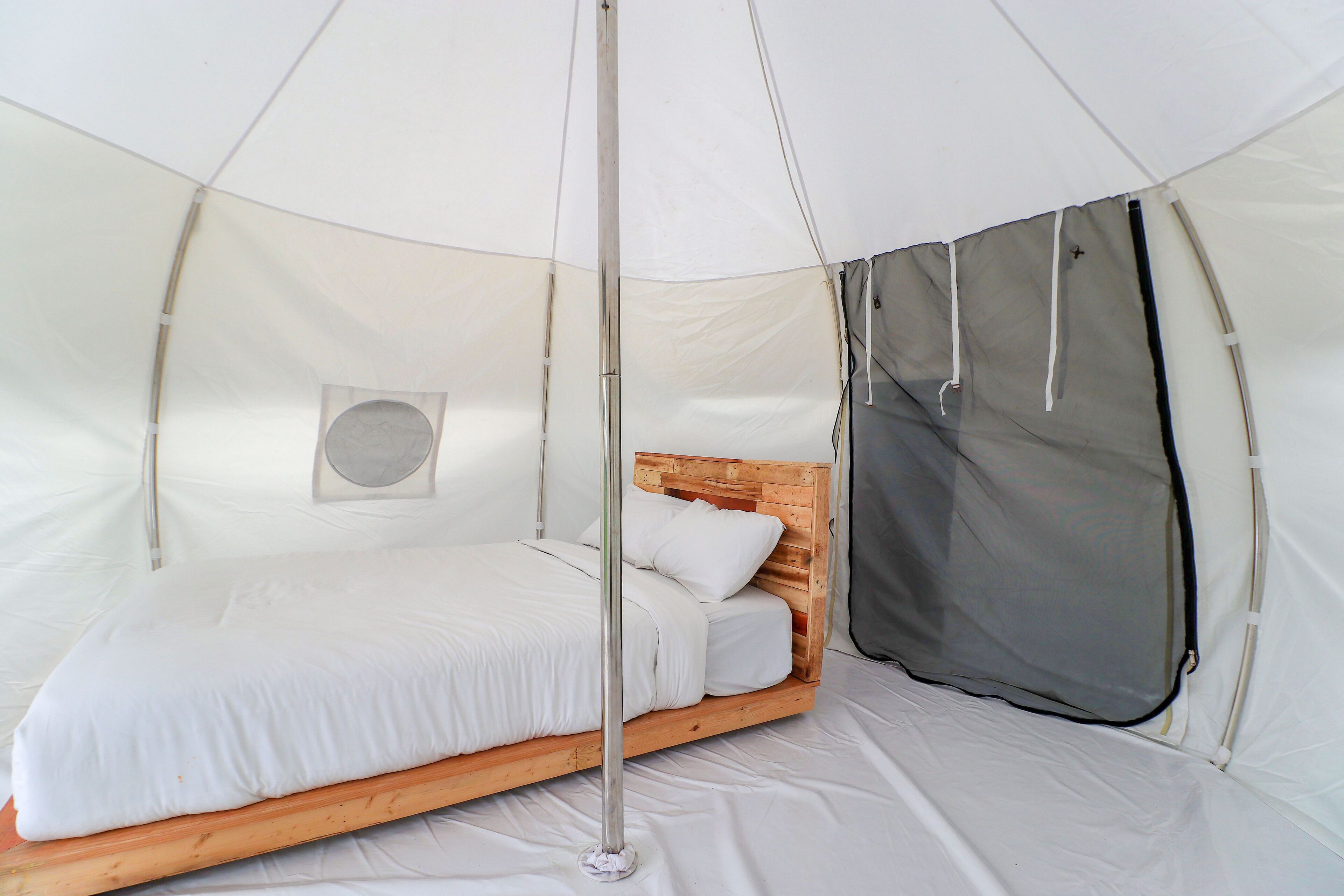 A tent with a bed, a metal pole, and a gray netting.