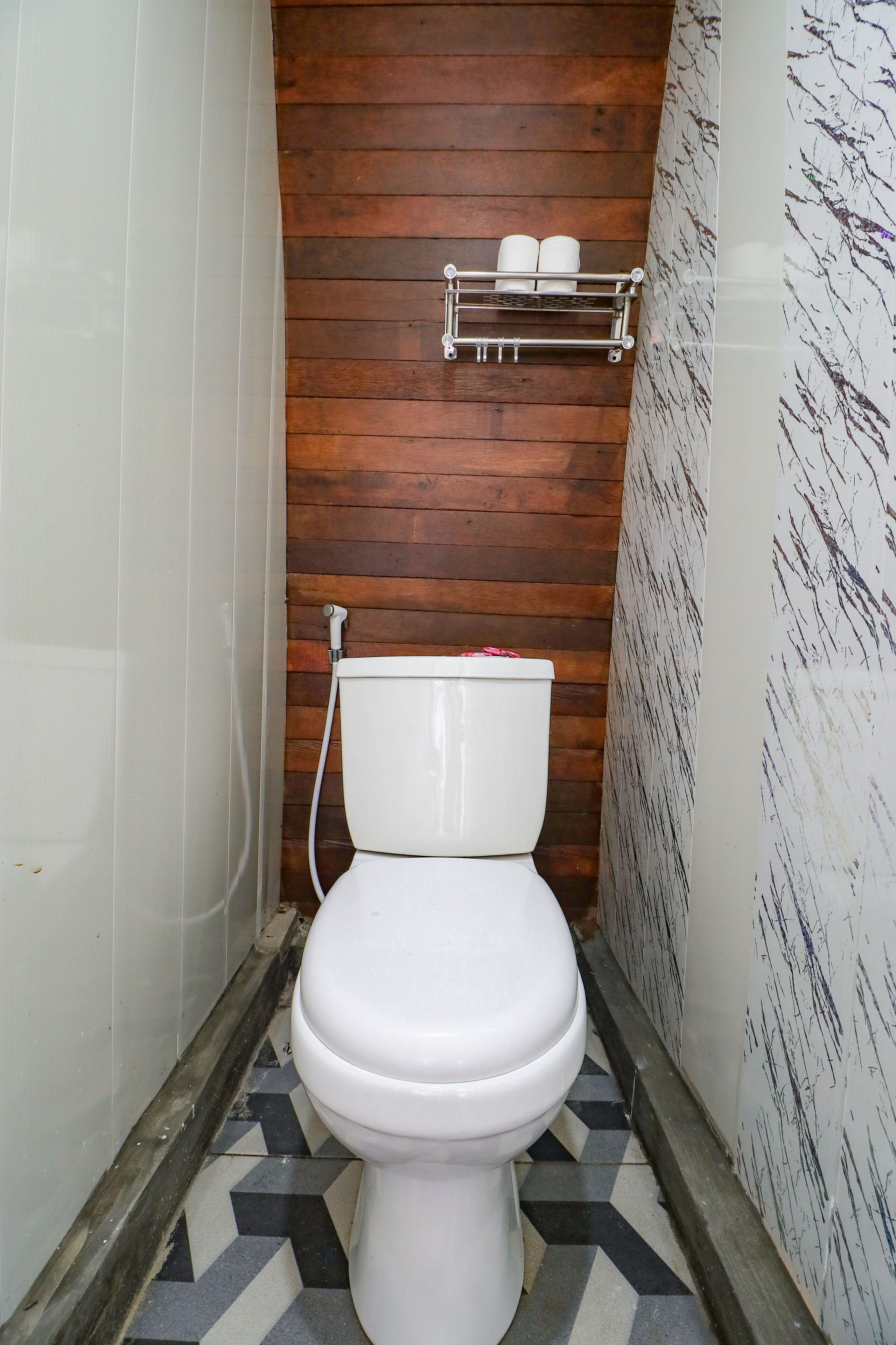 Un baño con inodoro blanco, pared de paneles de madera y suelo de baldosas.