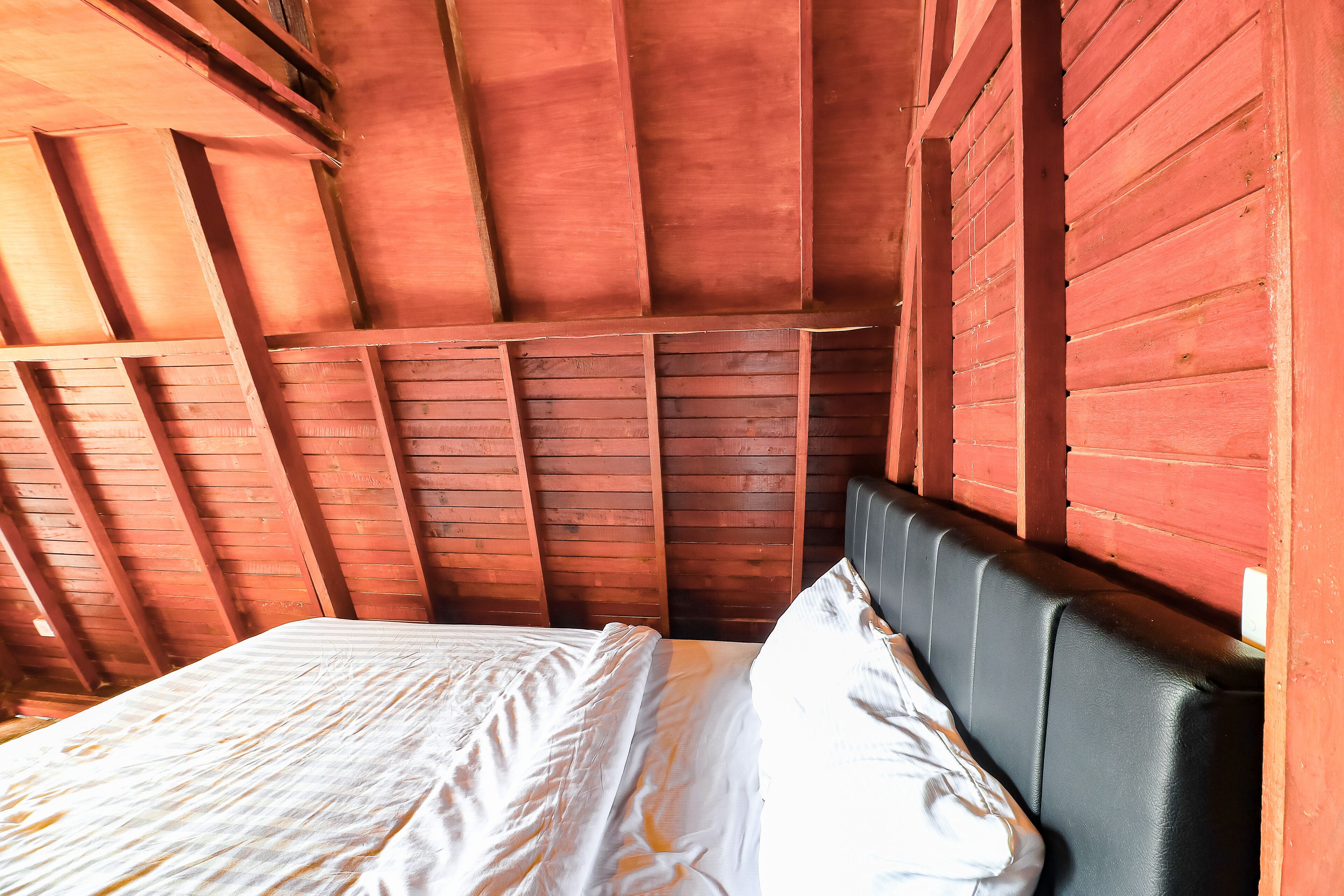 A wooden room with a bed against the wall, a sloped ceiling, and a window.