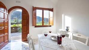 A dining area with a table set for two, a window with wooden shutters, and a view of a mountainous landscape.