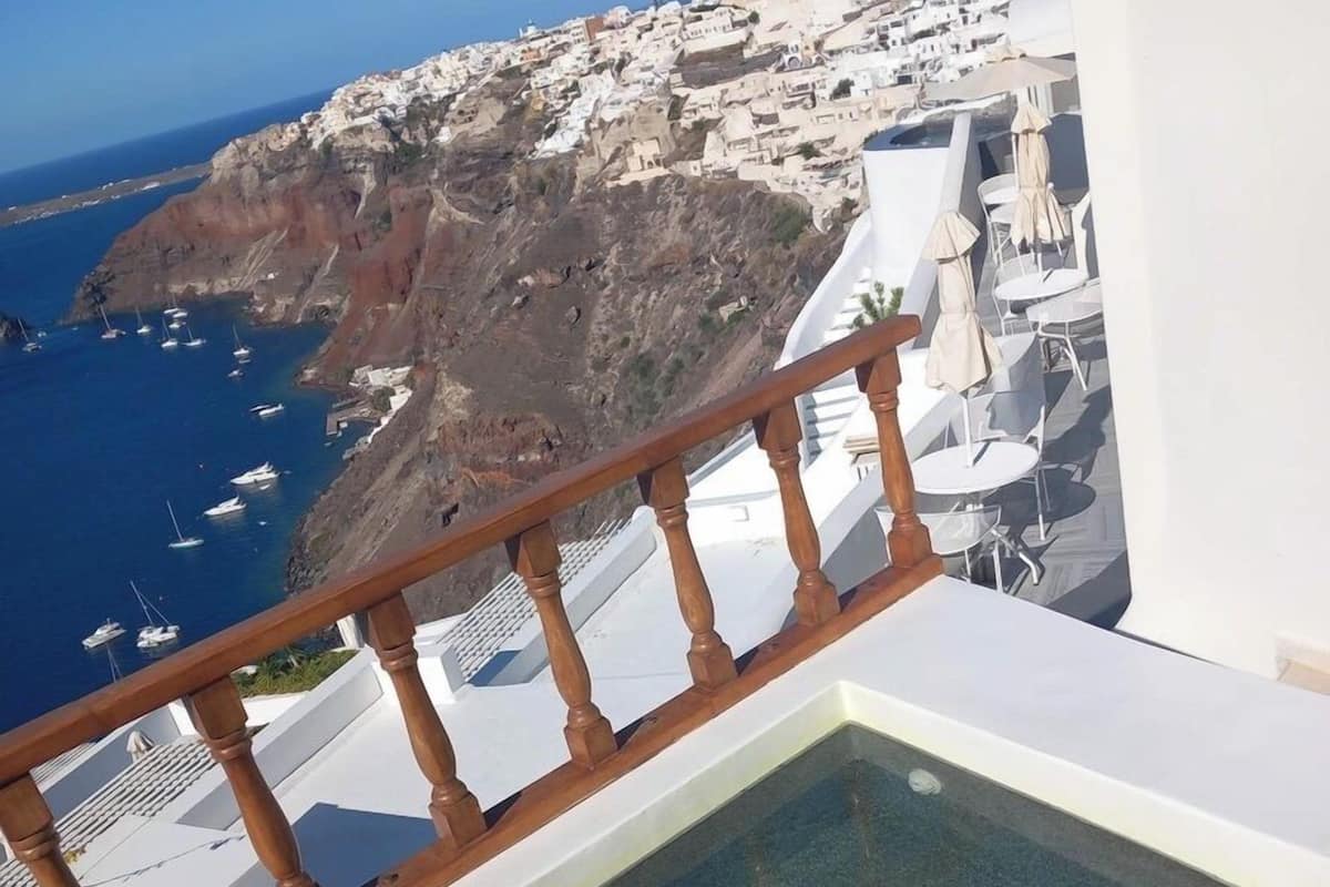 A balcony with a wooden railing overlooking a coastal town with white buildings and a clear blue sea.