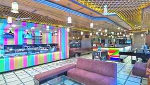 A brightly lit bar area with colorful vertical stripes, cushioned seating, and a glass coffee table. - Hari Piorko Grand (New Delhi)