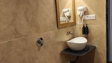 Un baño con inodoro blanco, lavamanos con recipiente, secador de pelo de pared y ducha con cabezal de ducha manual.