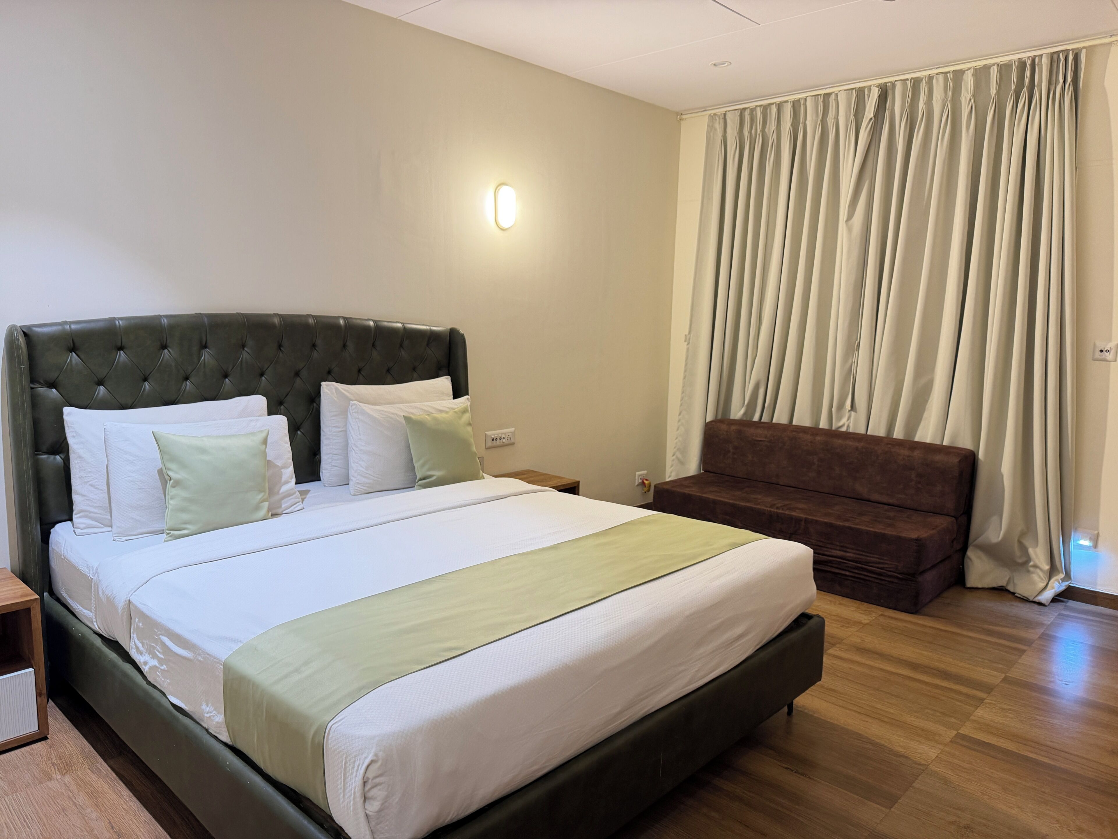 Un dormitorio con una cama, una mesita de noche, un sofá y una ventana con cortinas.