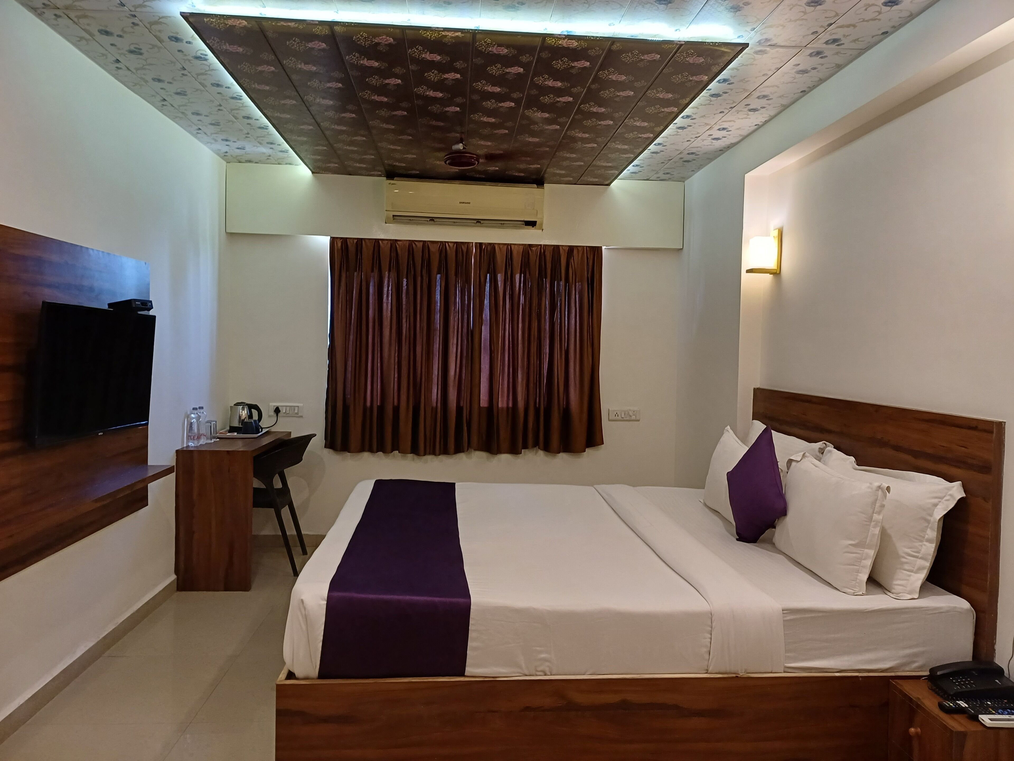 Una habitación de hotel con cama, escritorio, televisor y ventilador de techo.