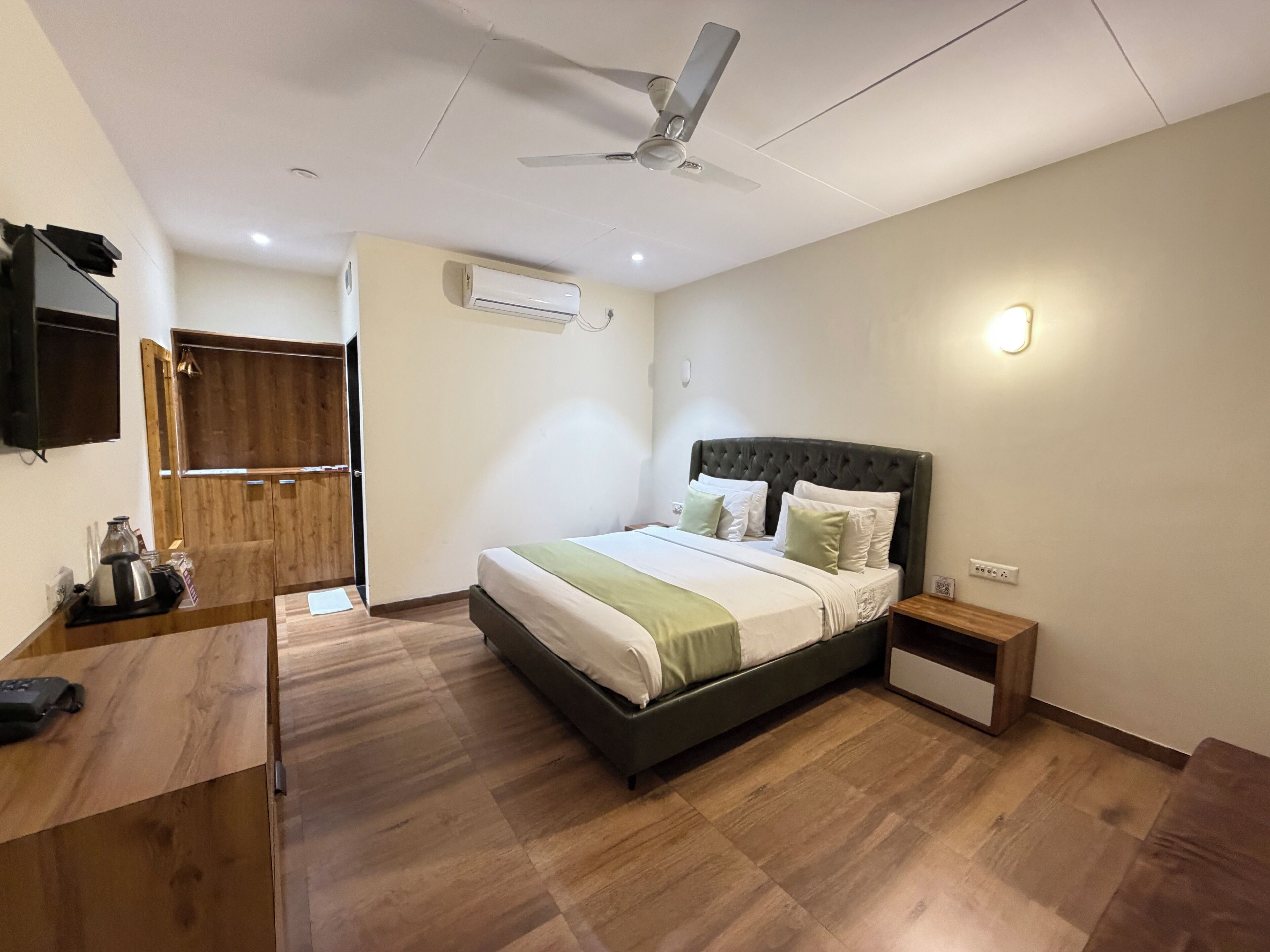 Un dormitorio con cama, escritorio de madera, armario, ventilador de techo y aire acondicionado.