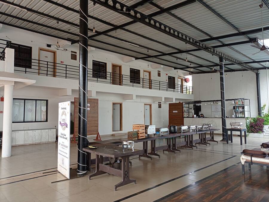 A spacious hall with multiple tables and benches, a high ceiling with metal beams, and a balcony on the upper level.