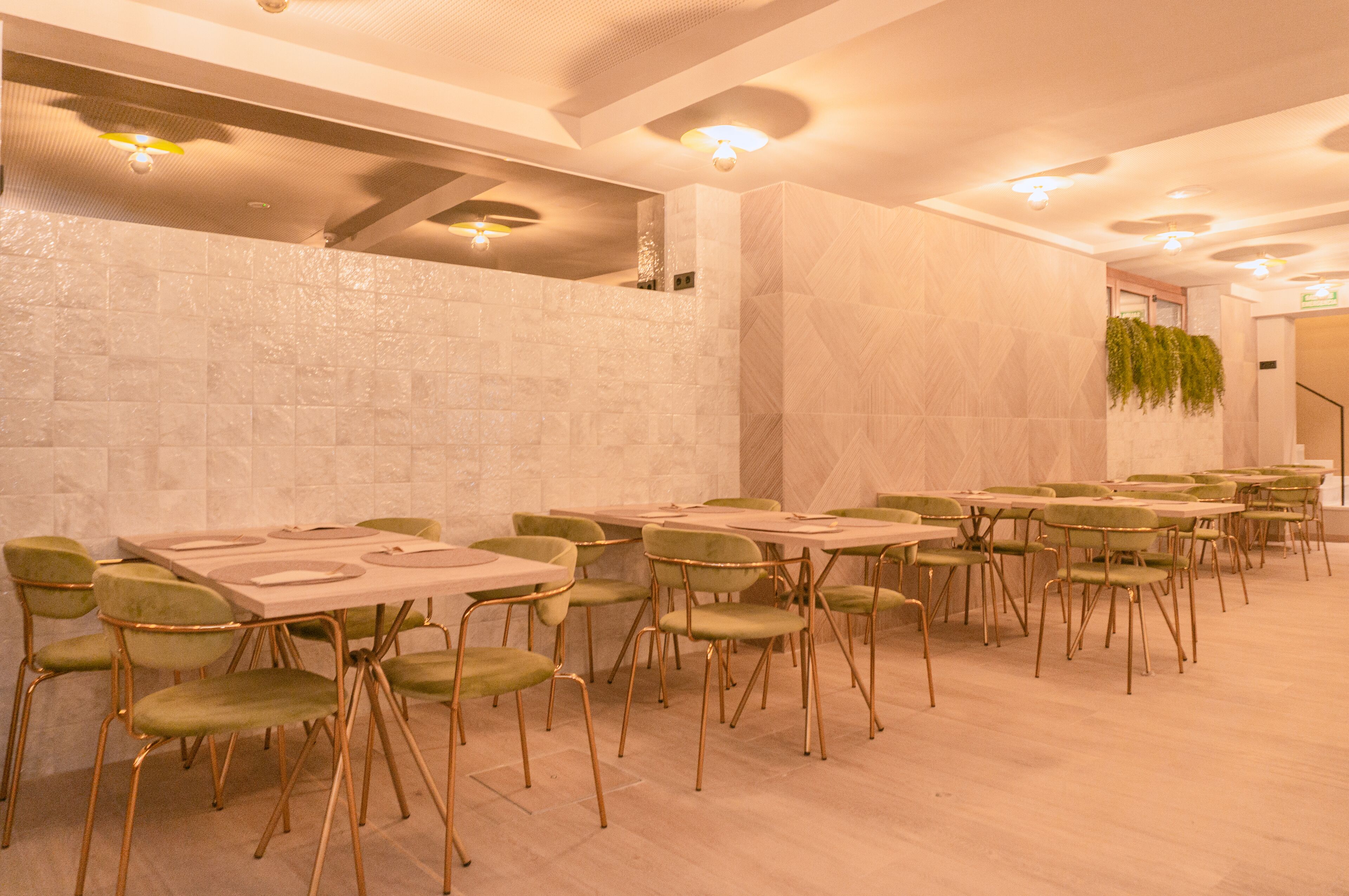Un comedor con varias mesas y sillas, un muro de piedra e iluminación empotrada en el techo.