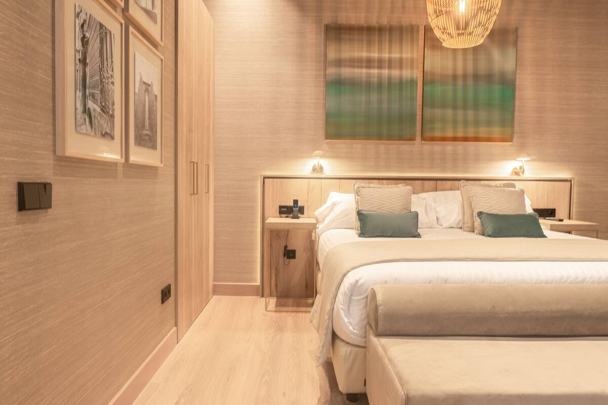 A modern bedroom with a large bed, bedside tables, and framed artwork on the wall.