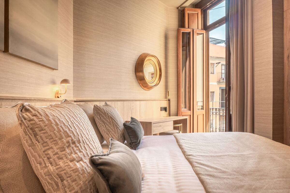 A hotel room with a large bed, a desk, and a mirror on the wall.
