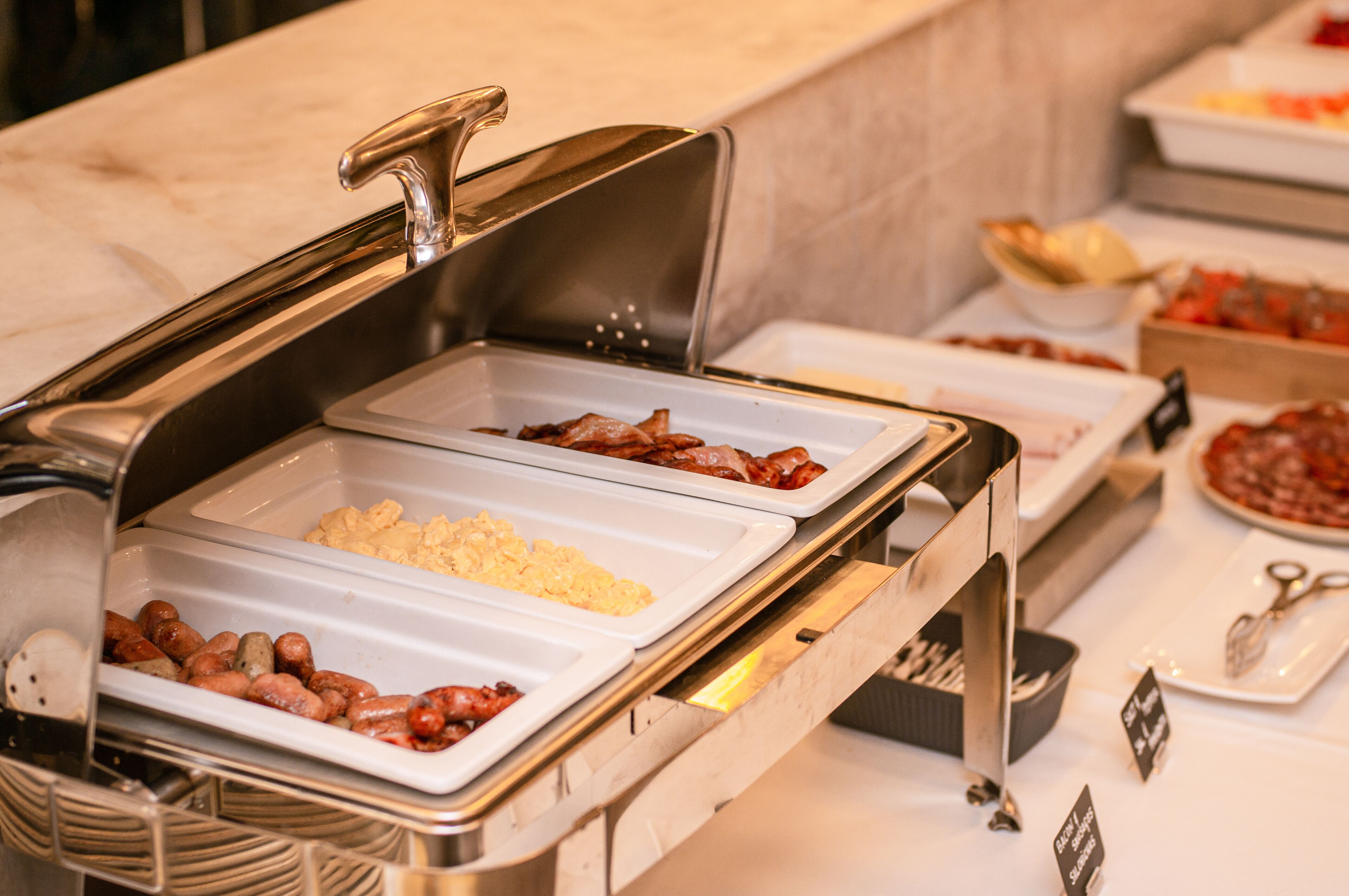 Un bufé con diversas opciones de comida, incluyendo salchichas, huevos revueltos y otros platos.