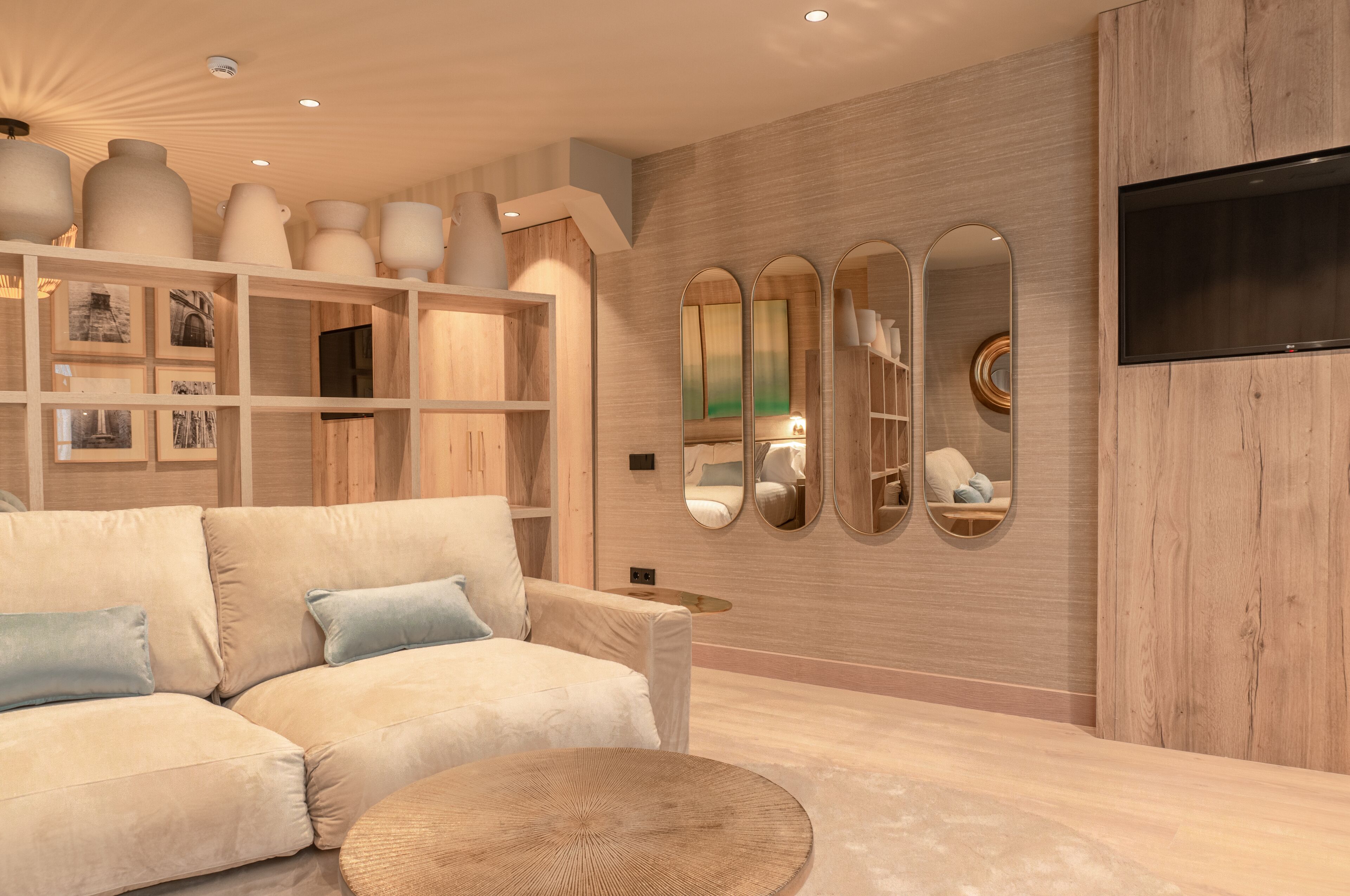 Ein modernes Wohnzimmer mit einem beigen Sofa, einem runden Couchtisch und einer Holzwand mit eingebauten Regalen, auf denen dekorative Gegenstände präsentiert werden.