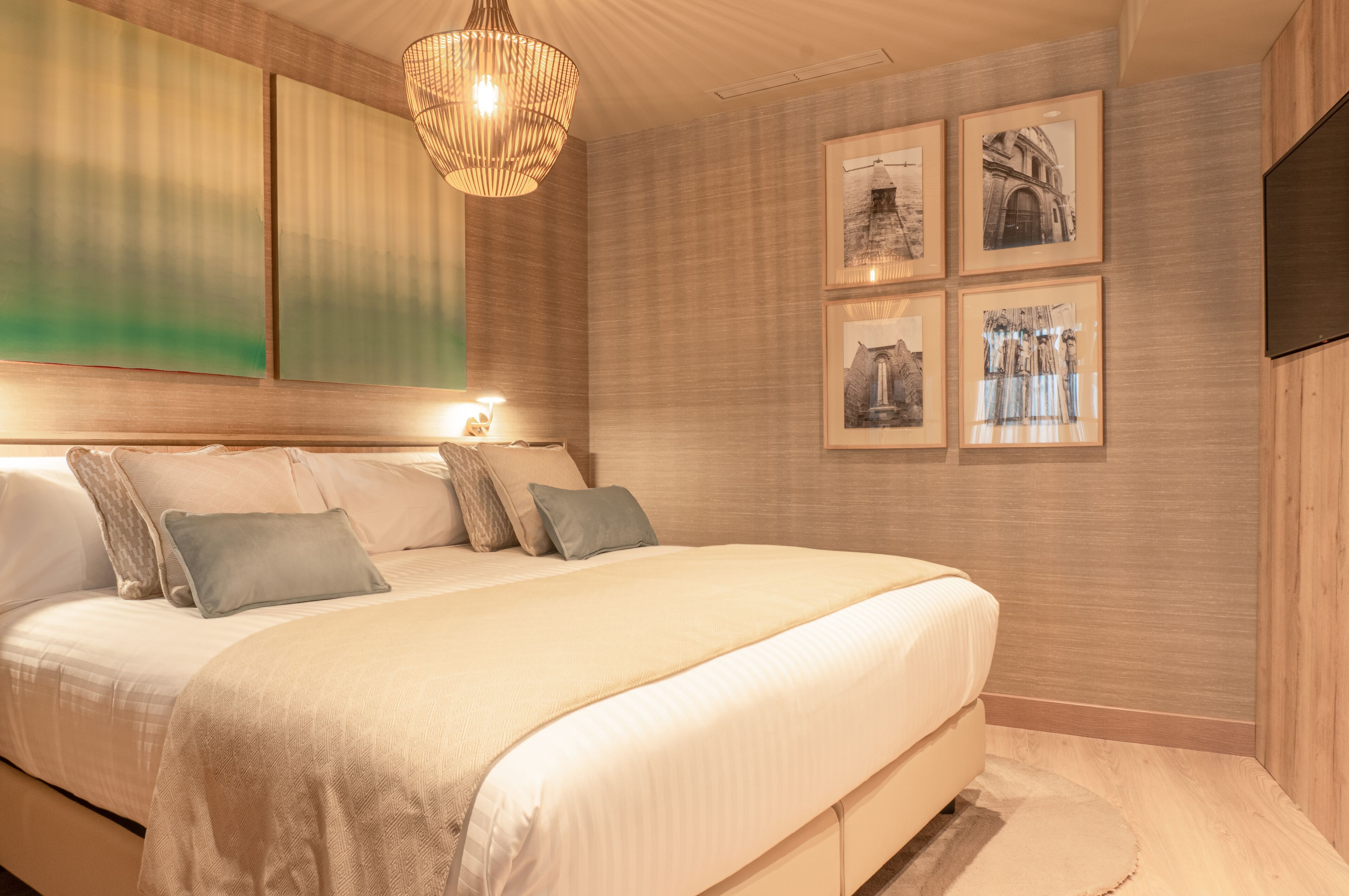 Un dormitorio con una cama grande, un cabecero de madera, una lámpara colgante y cuadros enmarcados en la pared.