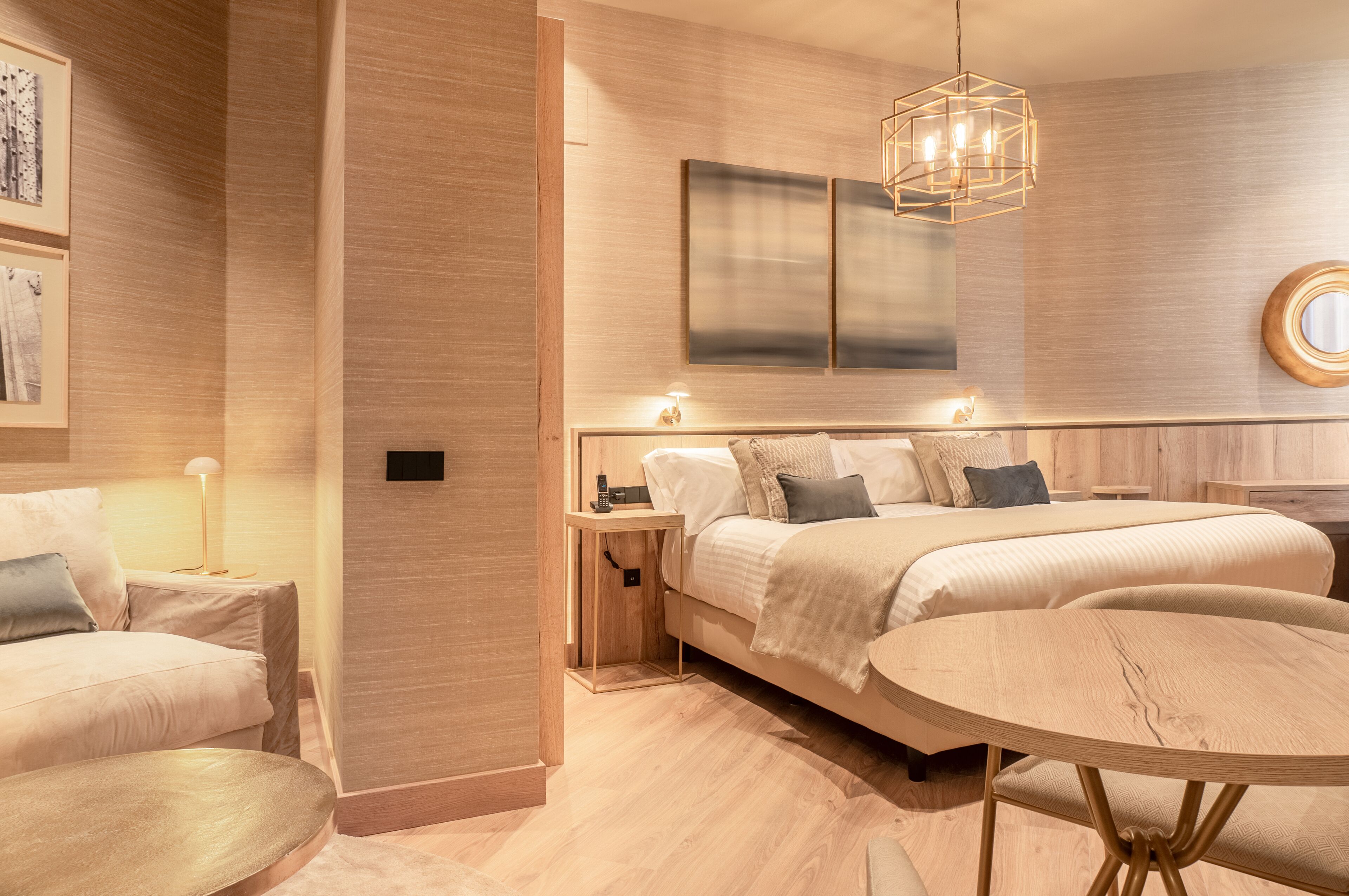 Un dormitorio moderno con una cama grande, mesitas de noche, una mesa redonda y una lámpara colgante.