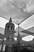 Un edificio histórico con un campanario y una estructura moderna con estructura metálica en primer plano.