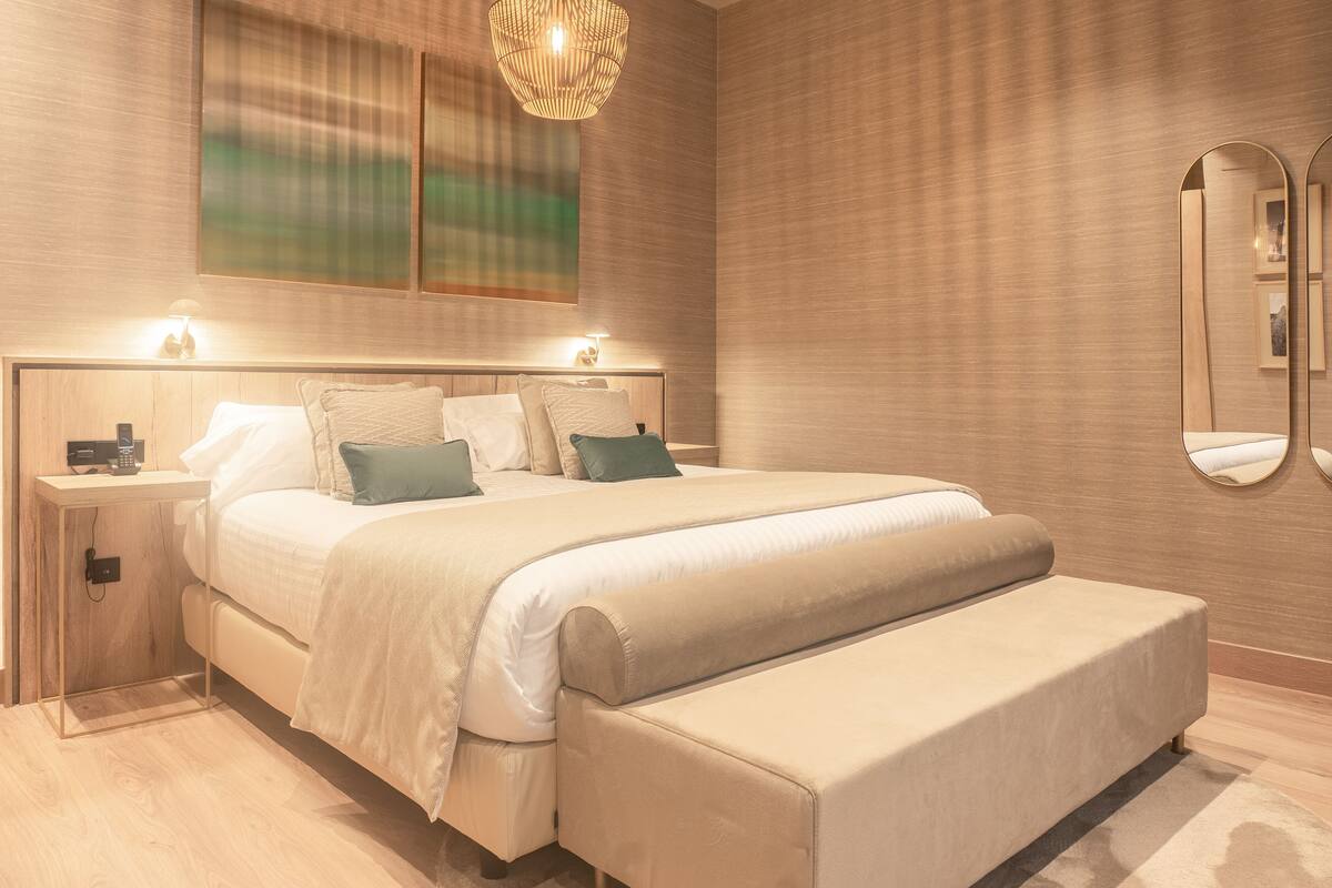 A modern bedroom with a large bed, bedside tables, a bedside lamp, and a mirror on the wall.