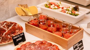 Un bufé con diferentes opciones de comida, incluyendo jamón serrano, ensalada de tomate y embutidos.