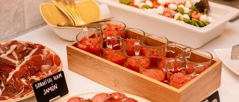 Un bufé con diferentes opciones de comida, incluyendo jamón serrano, ensalada de tomate y embutidos.