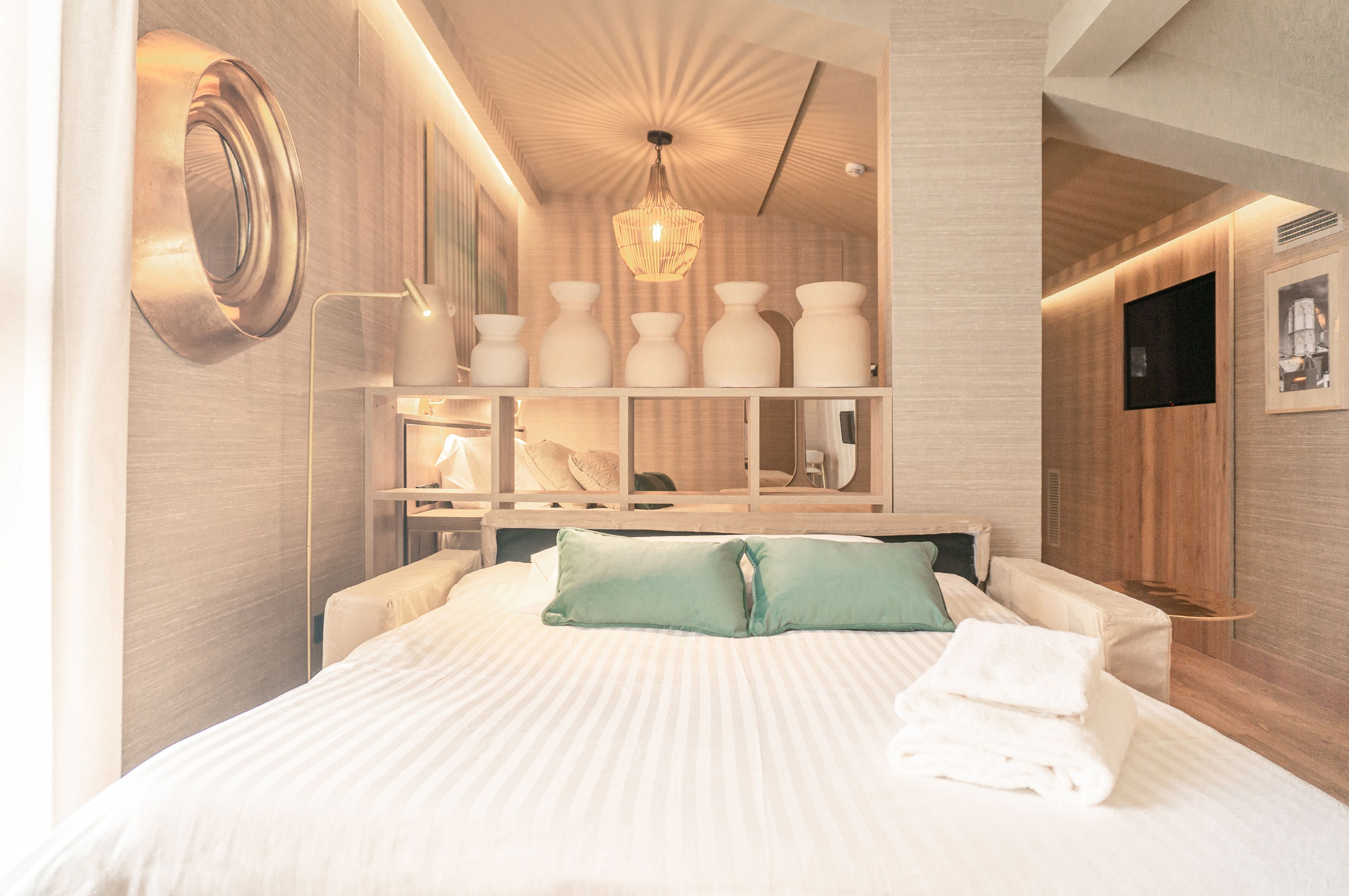 Een moderne hotelkamer met een groot bed, een nachtkastje, een inbouwplank met decoratieve objecten, en een plafondlamp.