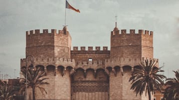 Una antigua puerta de piedra con dos torres, palmeras y gente caminando al frente.