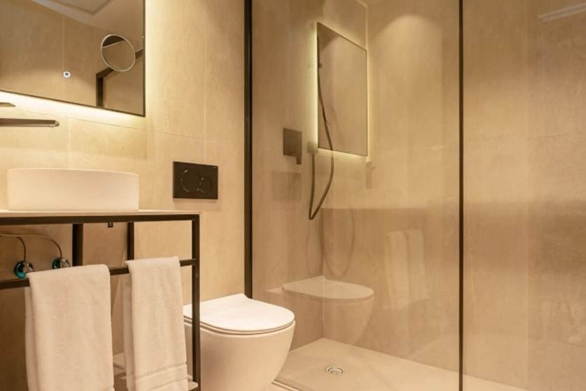 A modern bathroom with a glass shower enclosure, a white toilet, and a sink with a mirror above it.
