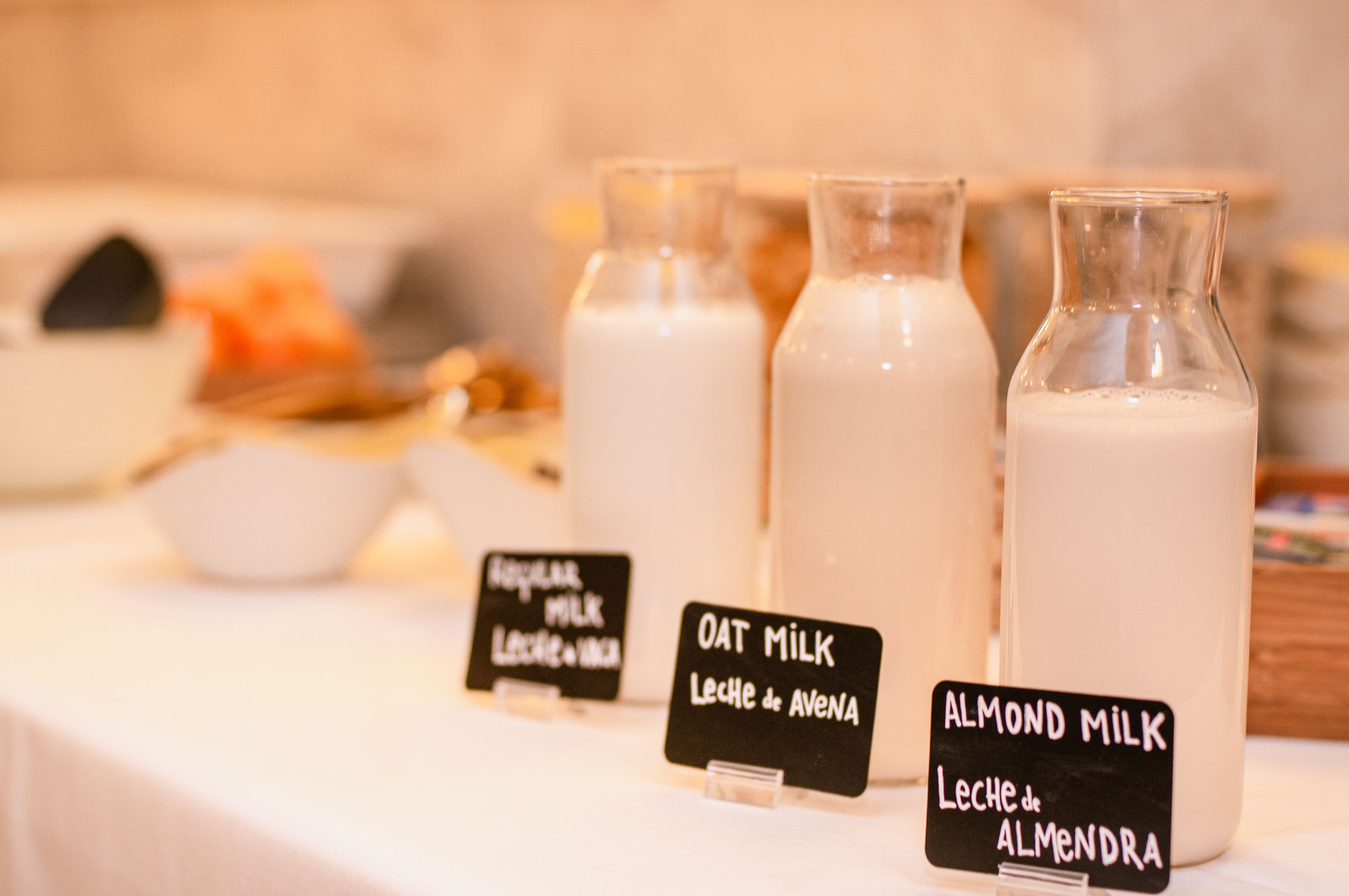 Una mesa con tres botellas etiquetadas de leche, un bol de nueces y un cartel que indica los tipos de leche disponibles.