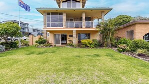 A two-story house with a balcony, a well-maintained lawn, and a flag. - Anchored at Fingal Bay, 80 Marine Drive (Fingal Bay)
