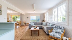 A spacious living room with a large sofa, a coffee table, and a dining area with chairs and a table. - Anchored at Fingal Bay, 80 Marine Drive (Fingal Bay)