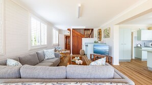 A spacious living room with a grey sofa, wooden flooring, and a TV on a stand. - Anchored at Fingal Bay, 80 Marine Drive (Fingal Bay)