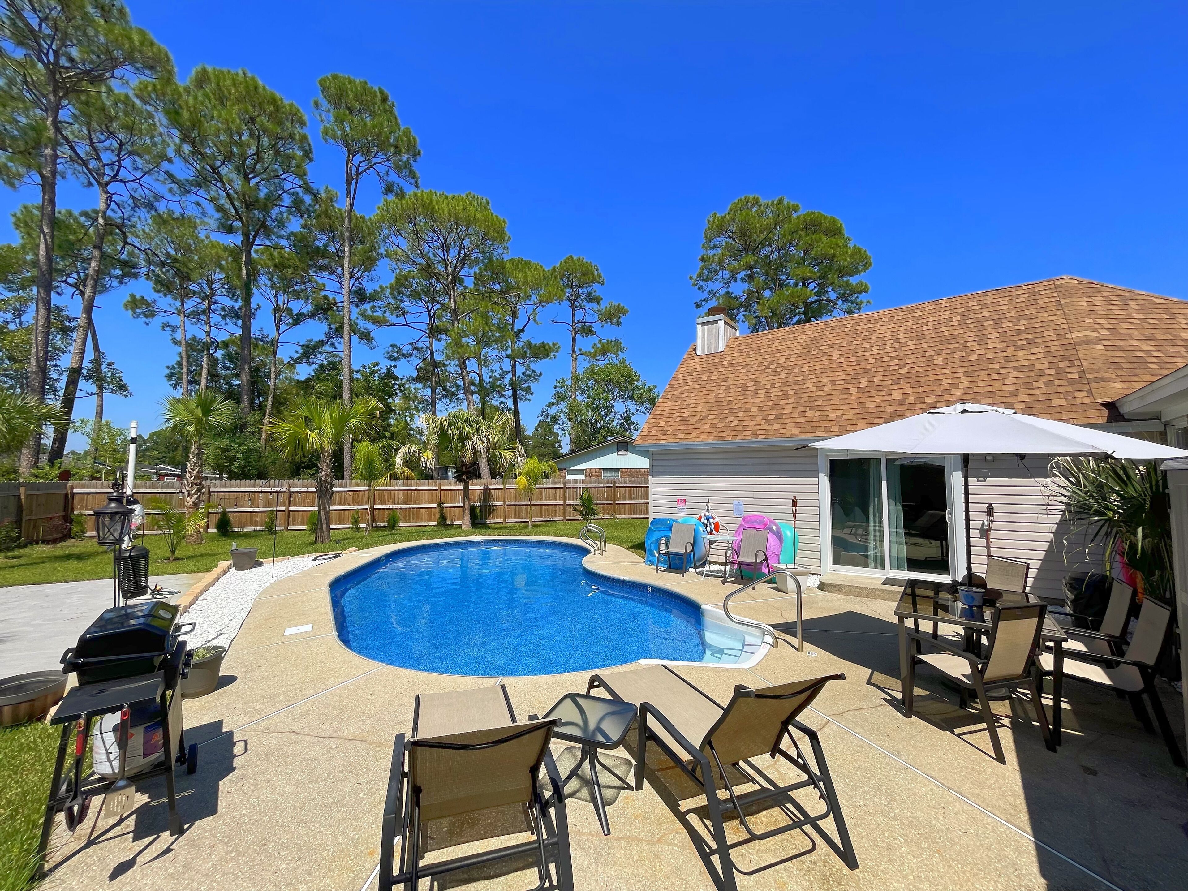 A backyard with a swimming pool, patio furniture, and a barbecue grill.