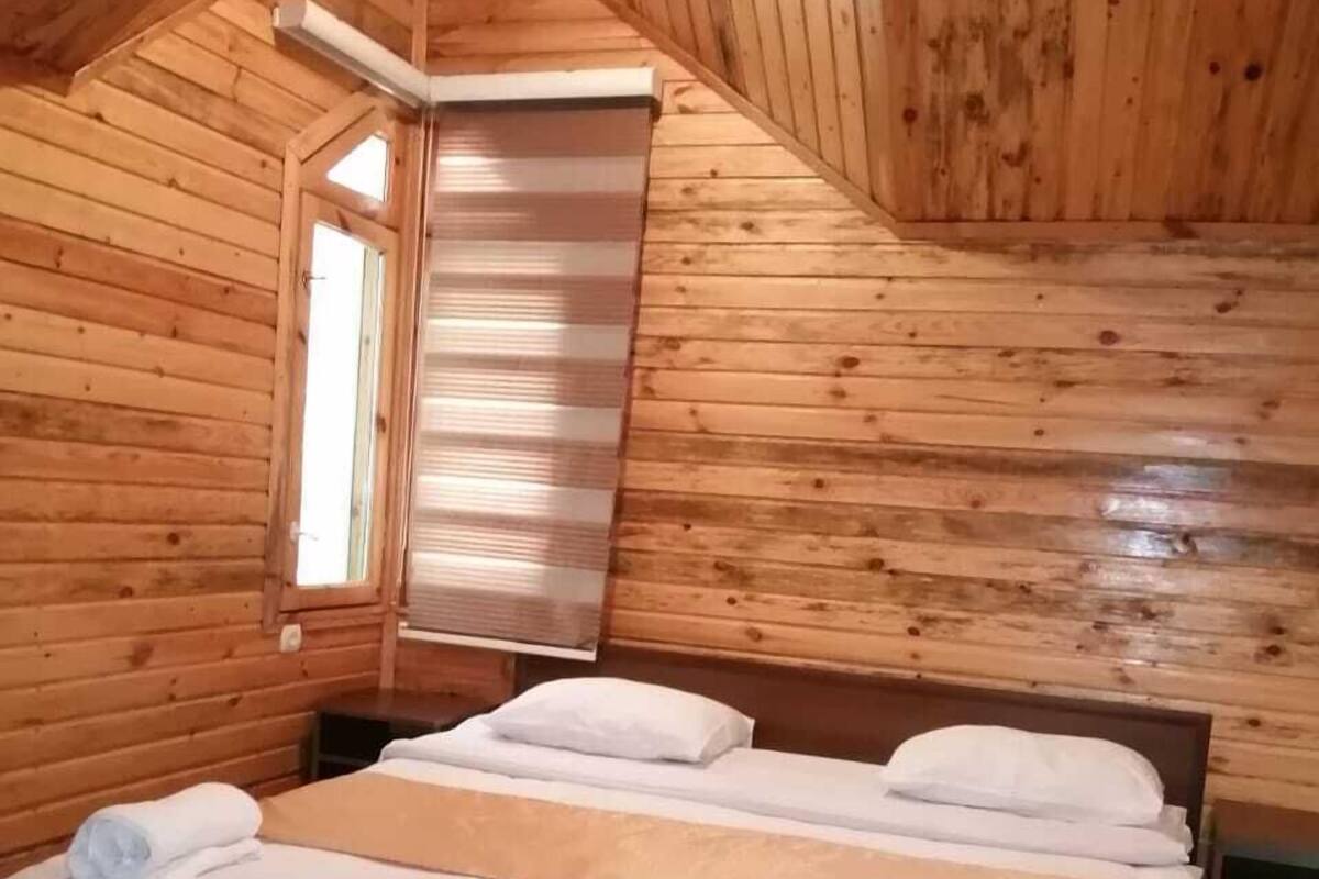 Ett sovrum i en stuga, inrett med träpanel, som innehåller en säng, två kuddar och ett fönster.