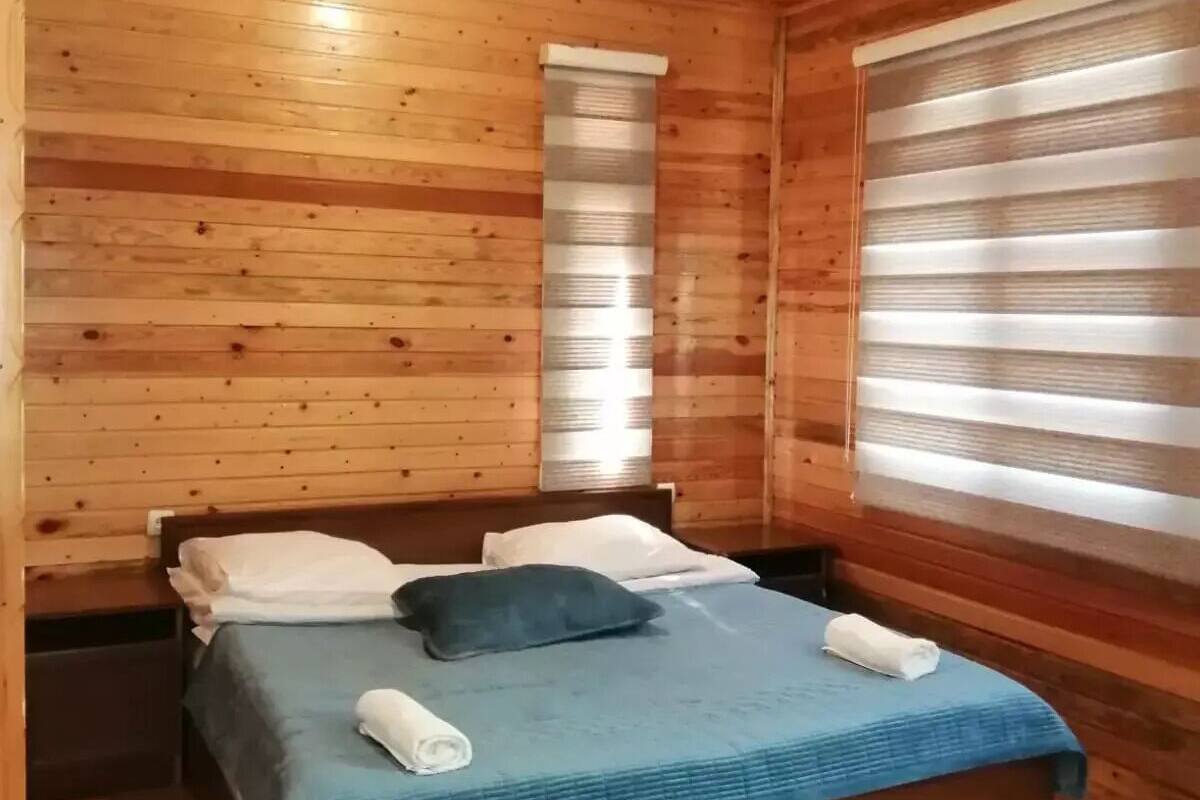 En stuga med träpanel, ett rum med en säng, kuddar och ett fönster med persienner.