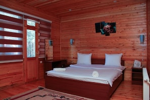 Une chambre dans une cabane en bois, avec un lit, des tables de chevet, un miroir et une fenêtre avec des stores.