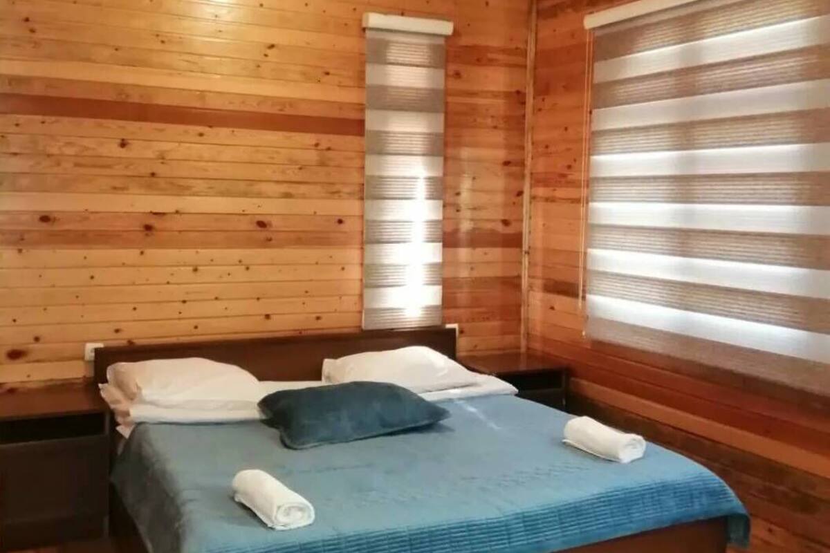 Ett sovrum i en stuga, inrett med träpanel, som innehåller en säng, kuddar och ett fönster med persienner.