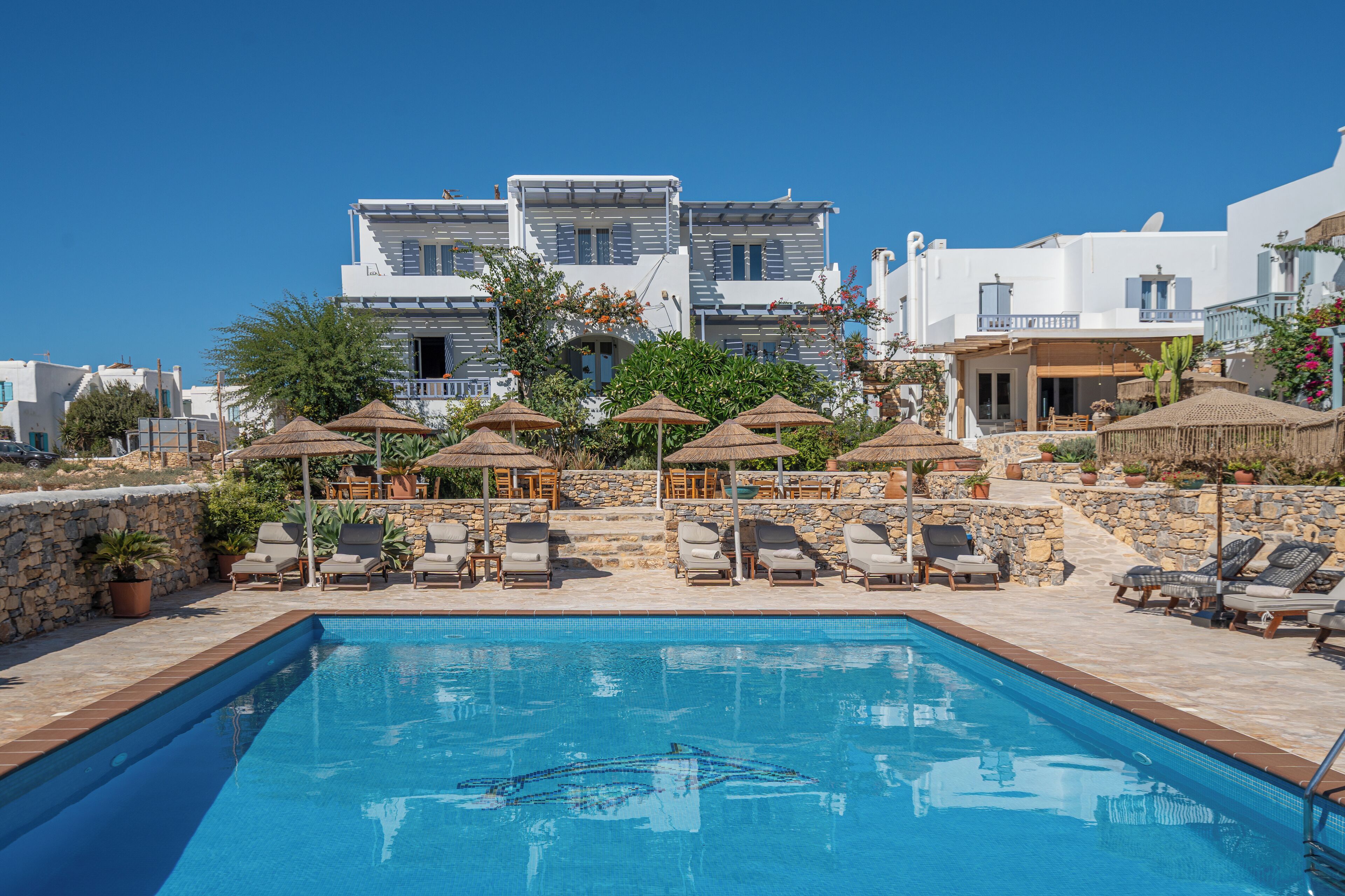 A pool area with lounge chairs and umbrellas, surrounded by stone walls and buildings with white facades.