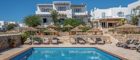 A pool area with lounge chairs and umbrellas, surrounded by stone walls and buildings with white facades.
