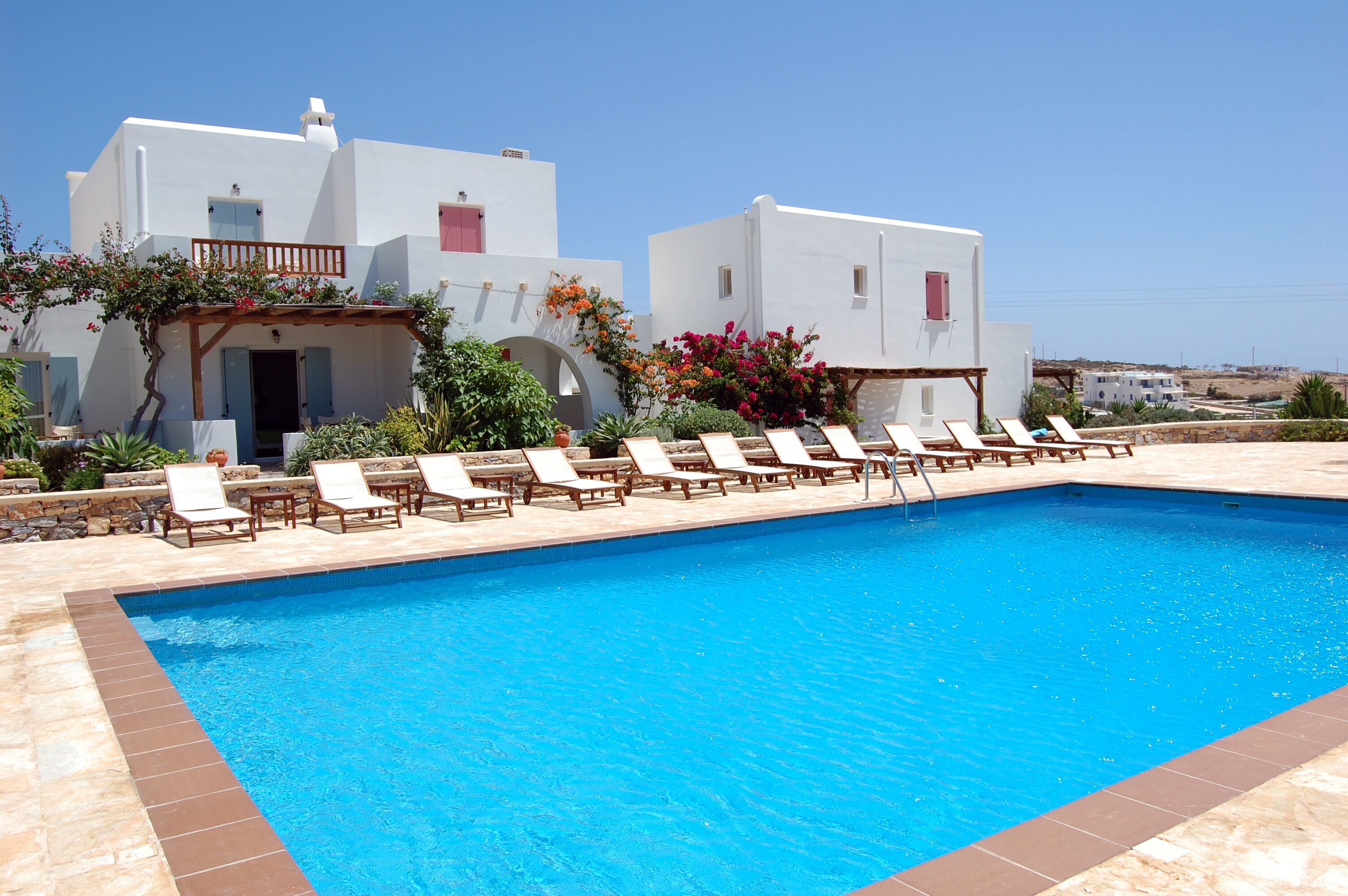 A pool area with lounge chairs and a building with white walls and red accents.