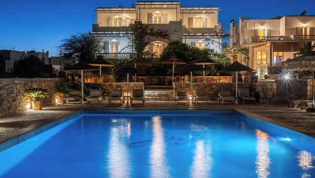 A swimming pool with lounge chairs and umbrellas, surrounded by stone walls and a building with multiple balconies. - Aeolos Hotel (Naxos)