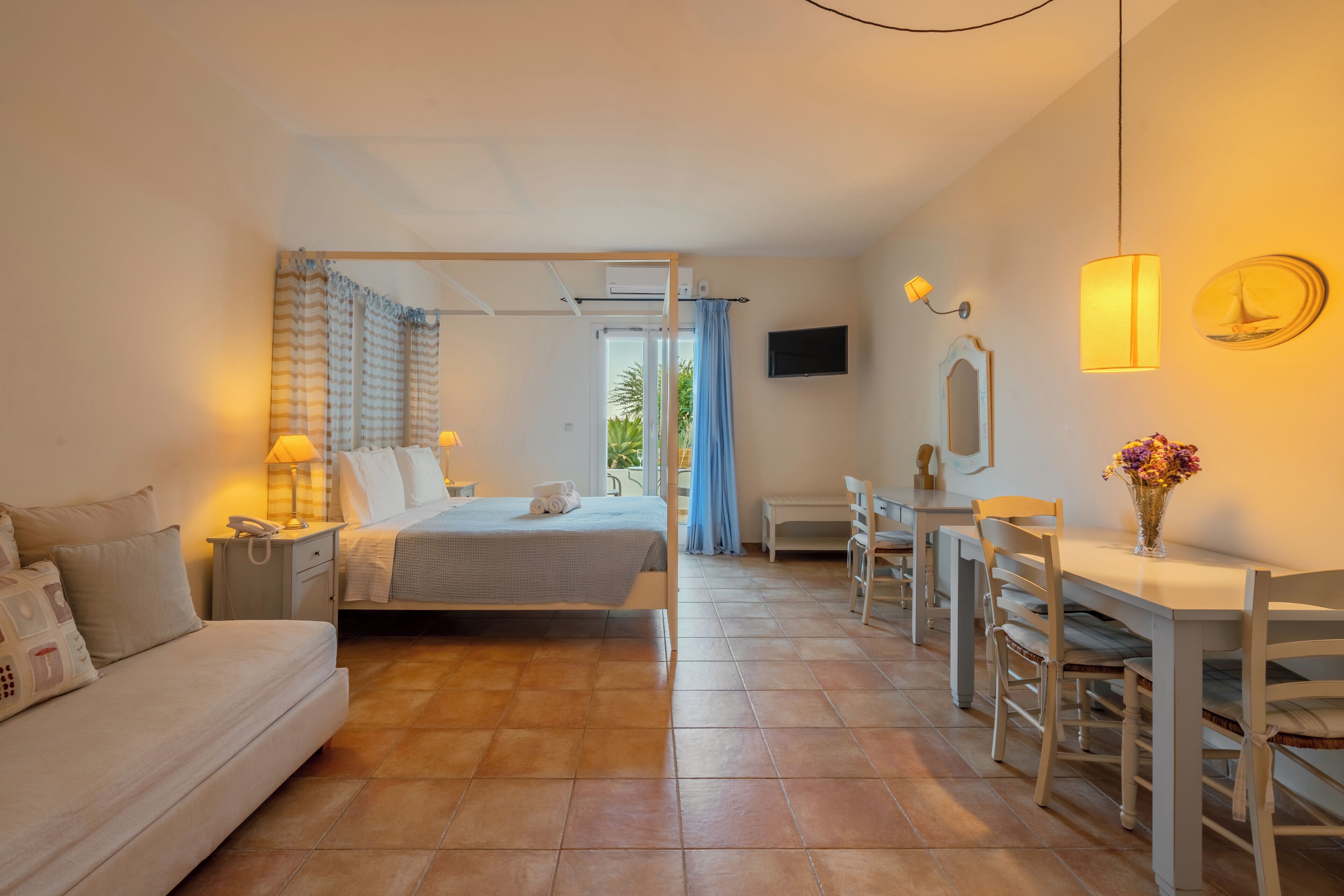 A hotel room with a bed, bedside table, lamp, and a view of the outdoors.