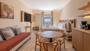 A modern hotel room with a sofa, a dining table, a bed, and a kitchen area. - Aeolos Hotel (Naxos)